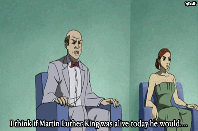 Gif shows a white man and white woman sitting in easy chairs on a stage. The white man is saying, "I think if Martin Luther King was alive today he would..." At this moment, a metal chair comes flying from out of the frame and knocks him and his chair backward. A black woman comes running after it and starts punching him. A television error screen saying PLEASE STAND BY pops up and ends the scene.